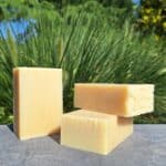 Savons solides Douce Avoine Milléniale sans étiquette, posés sur dallage gris avec décor végétal vert et ciel en arrière-plan.