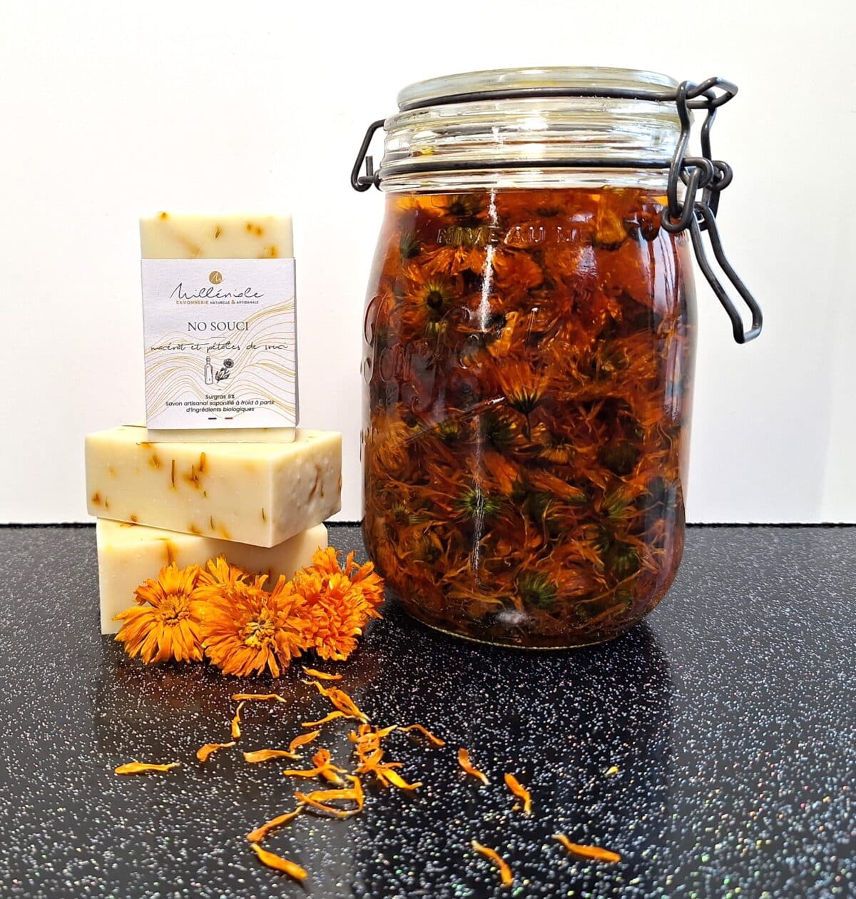Savons naturels No Souci au calendula Milléniale empilés avec fleurs de calendula et bocal de macérât de tournesol.
