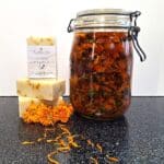 Savons naturels No Souci au calendula Milléniale empilés avec fleurs de calendula et bocal de macérât de tournesol.