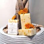Savons artisanaux No Souci au calendula Milléniale posés sur un pot de fleur avec arbuste et fleurs de souci.